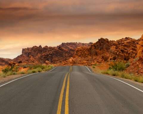 A highway leads to red rocks in the distance on an American hgihway.