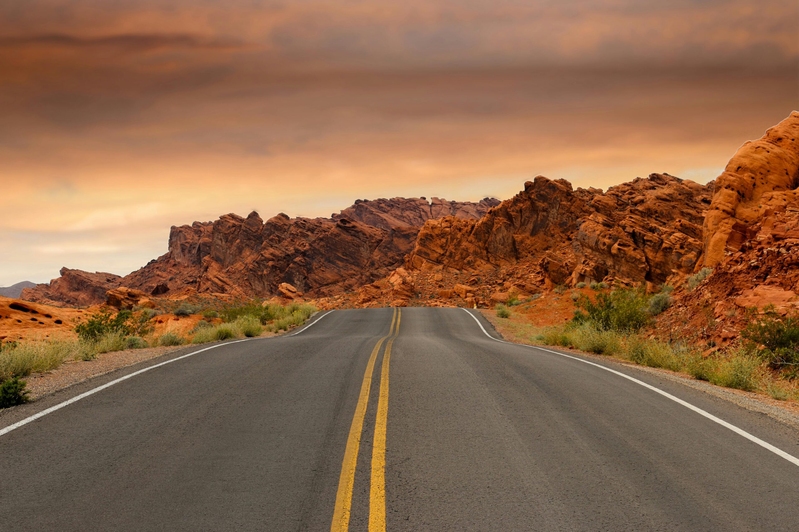 A highway leads to red rocks in the distance on an American hgihway.