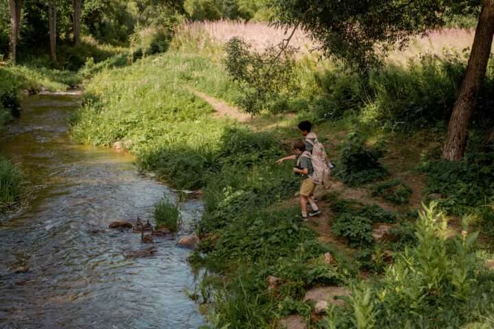 A grassy knoll alongside a creek with boy scouts playing.