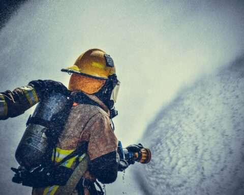 A firefighter dawning yellow and tan gear sprays a high-powered hose.