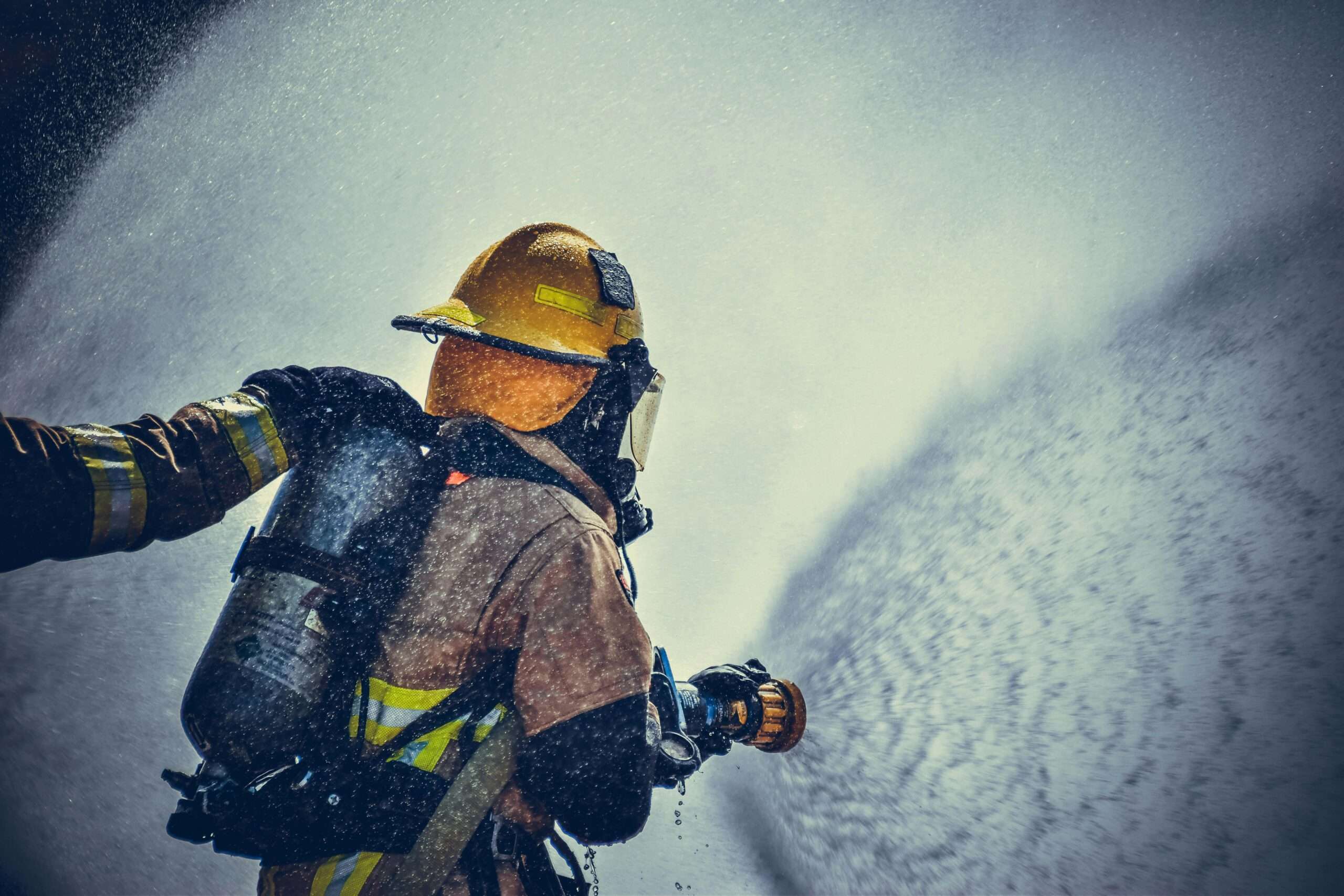 A firefighter dawning yellow and tan gear sprays a high-powered hose.