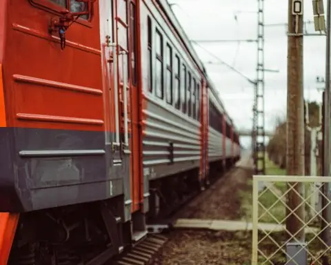 A red train sits on tracks nearby a railroad crossing.