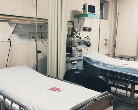 Two hopsital beds alongside a curtain and hopsital equipment.