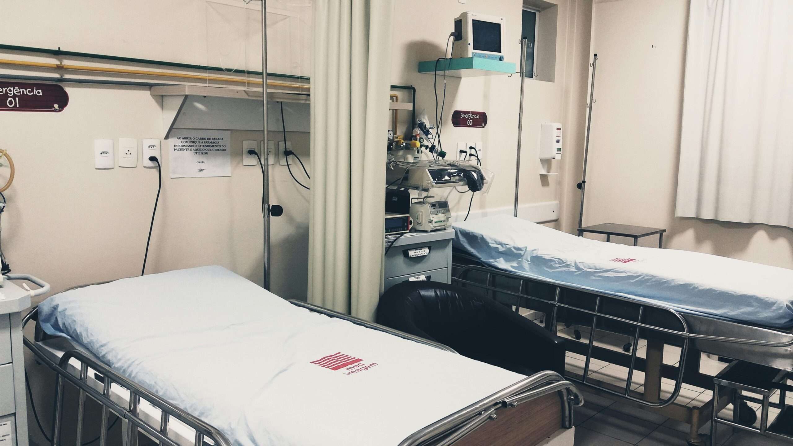 Two hopsital beds alongside a curtain and hopsital equipment.