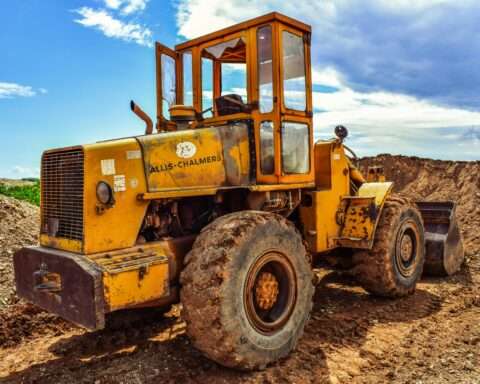 A bulldozer on a dirt mound before a blue sky.