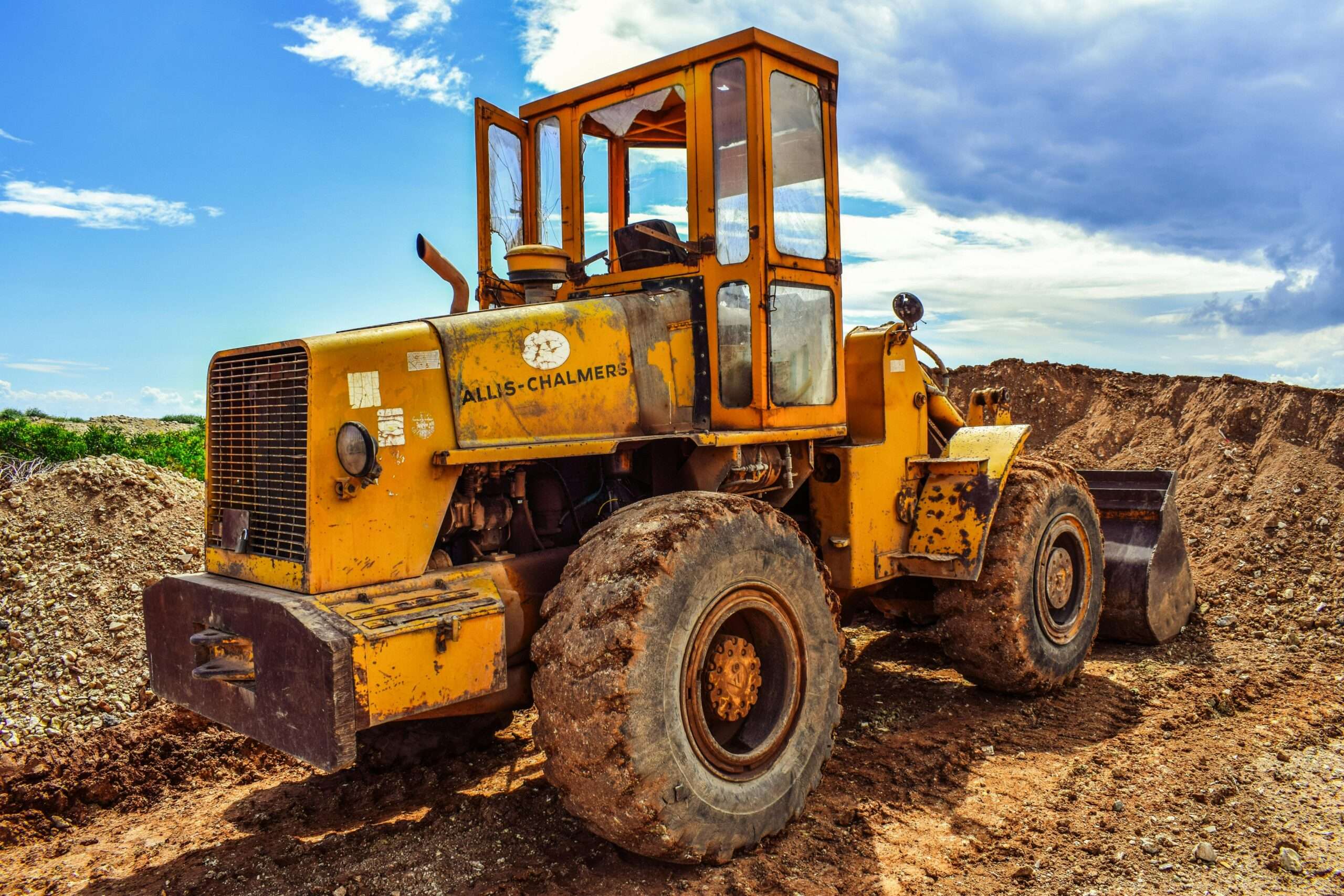 A bulldozer on a dirt mound before a blue sky.