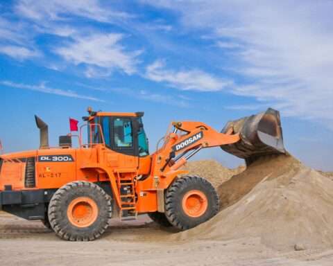 An orange bulldozer moving dirt before a blue sky.