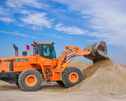 An orange bulldozer moving dirt before a blue sky.