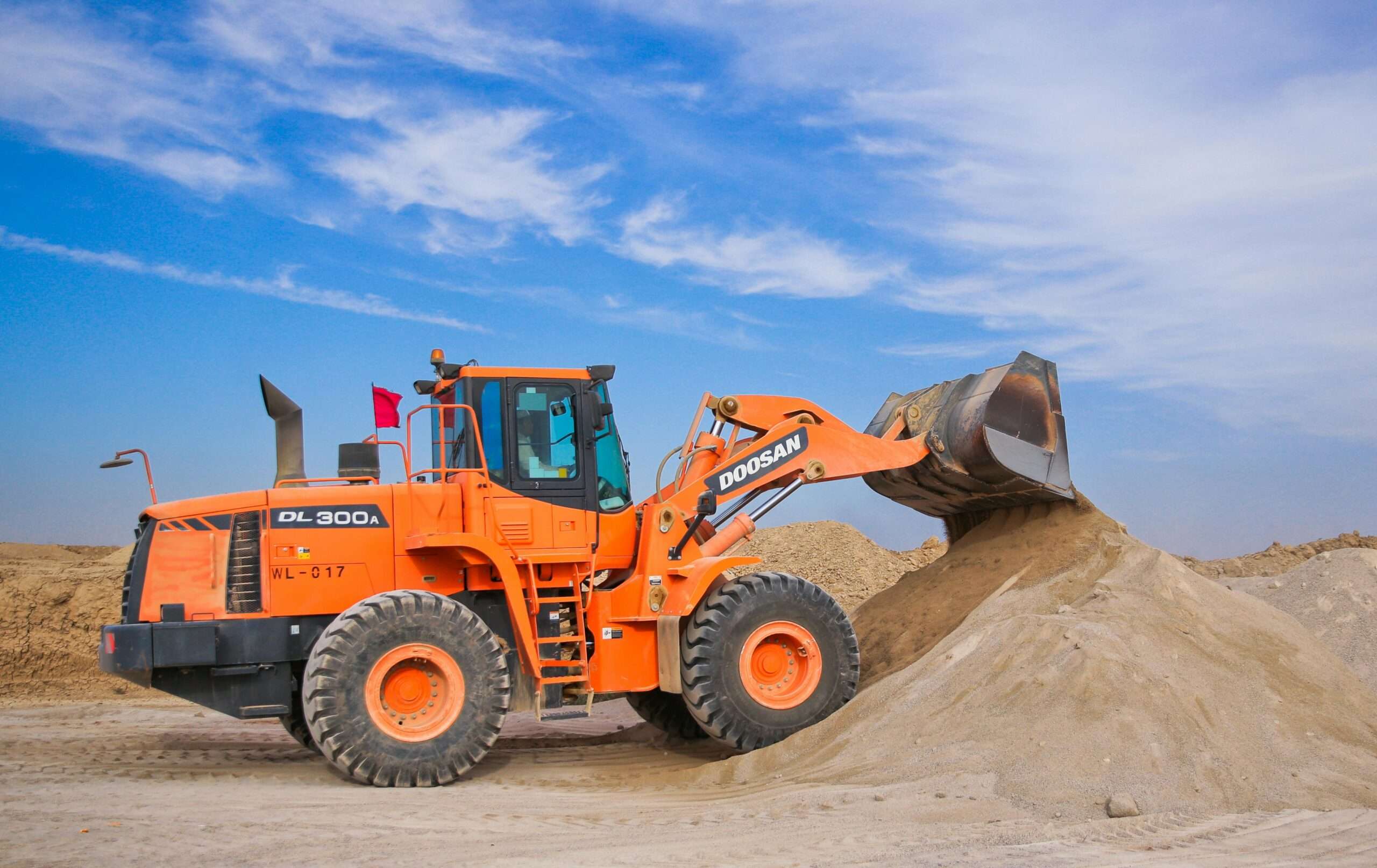 An orange bulldozer moving dirt before a blue sky.