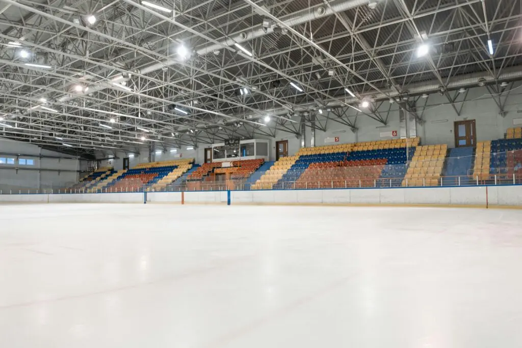 The inside of a hockey arena with colored seats and bright lights from ice level.