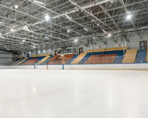 The inside of a hockey arena with colored seats and bright lights from ice level.