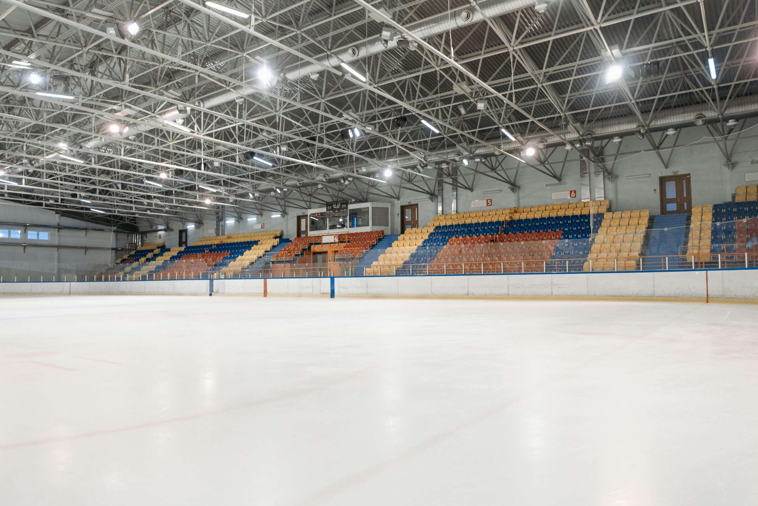 The inside of a hockey arena with colored seats and bright lights from ice level.