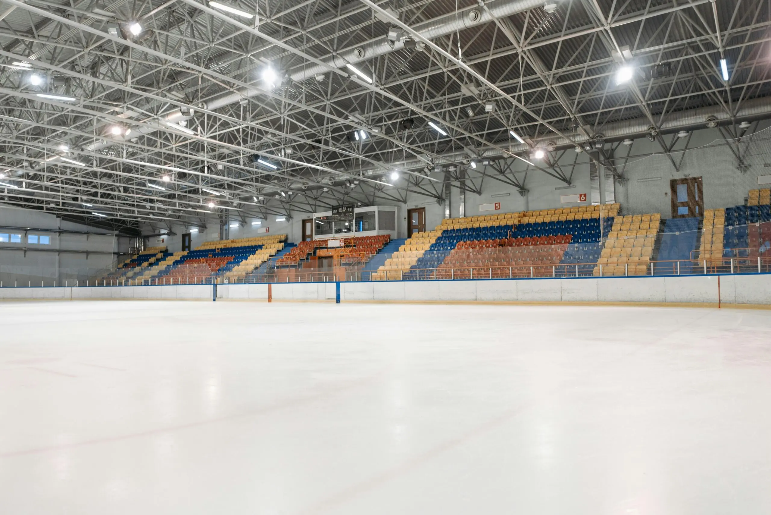 The inside of a hockey arena with colored seats and bright lights from ice level.
