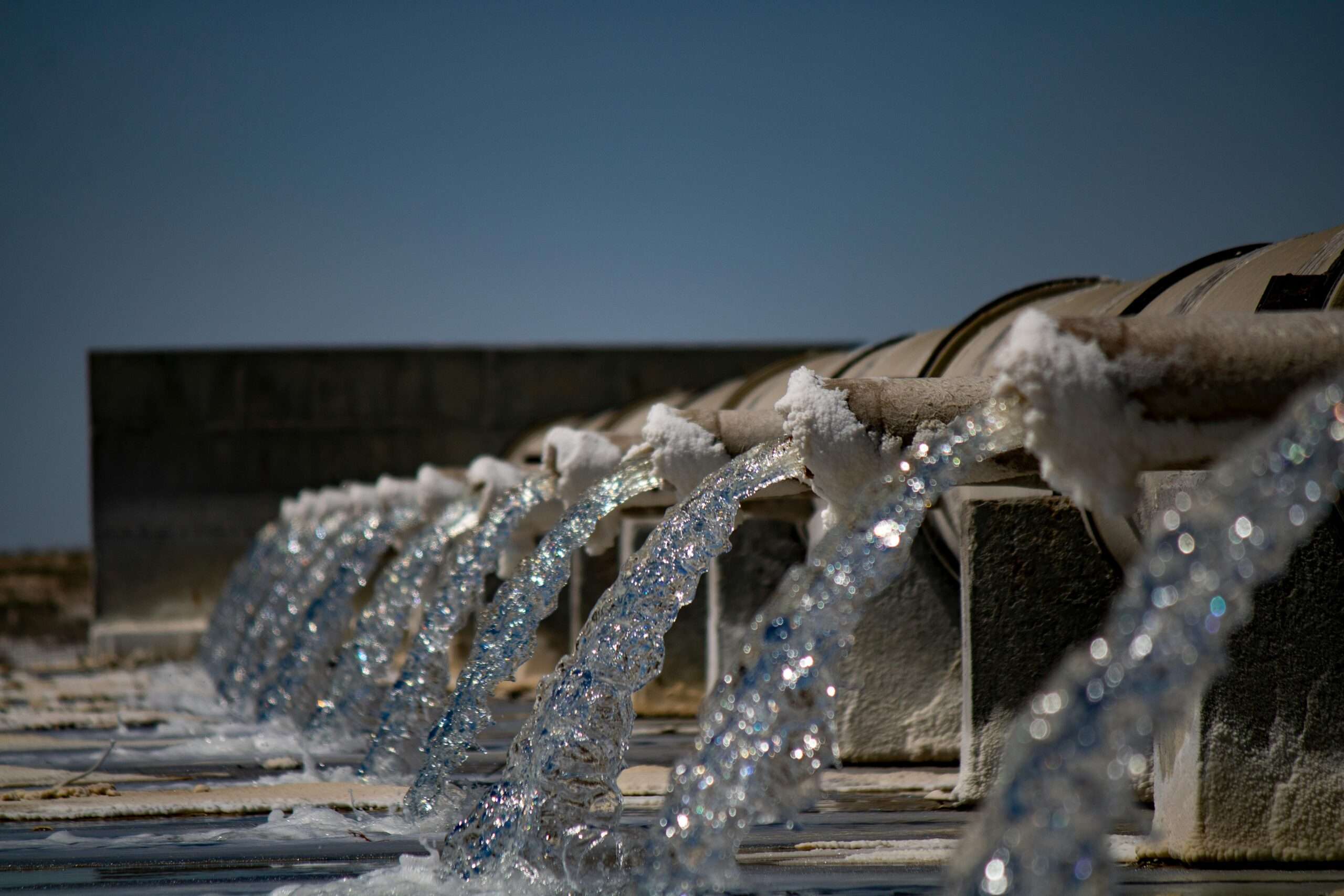 Several streams of water pour over pipes into a body of water.