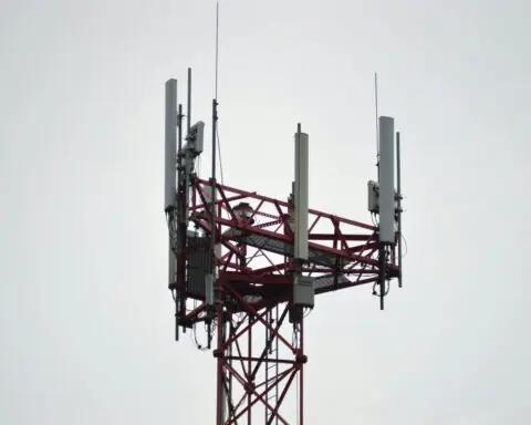 A 5G tower connecting residents and businesses to broadband internet service before a white cloudy sky.