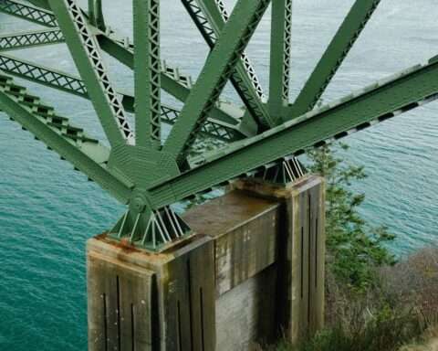 The underside of a bridge showing green arches supporting the bridge above water.