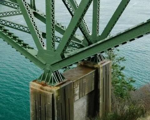The underside of a bridge showing green arches supporting the bridge above water.