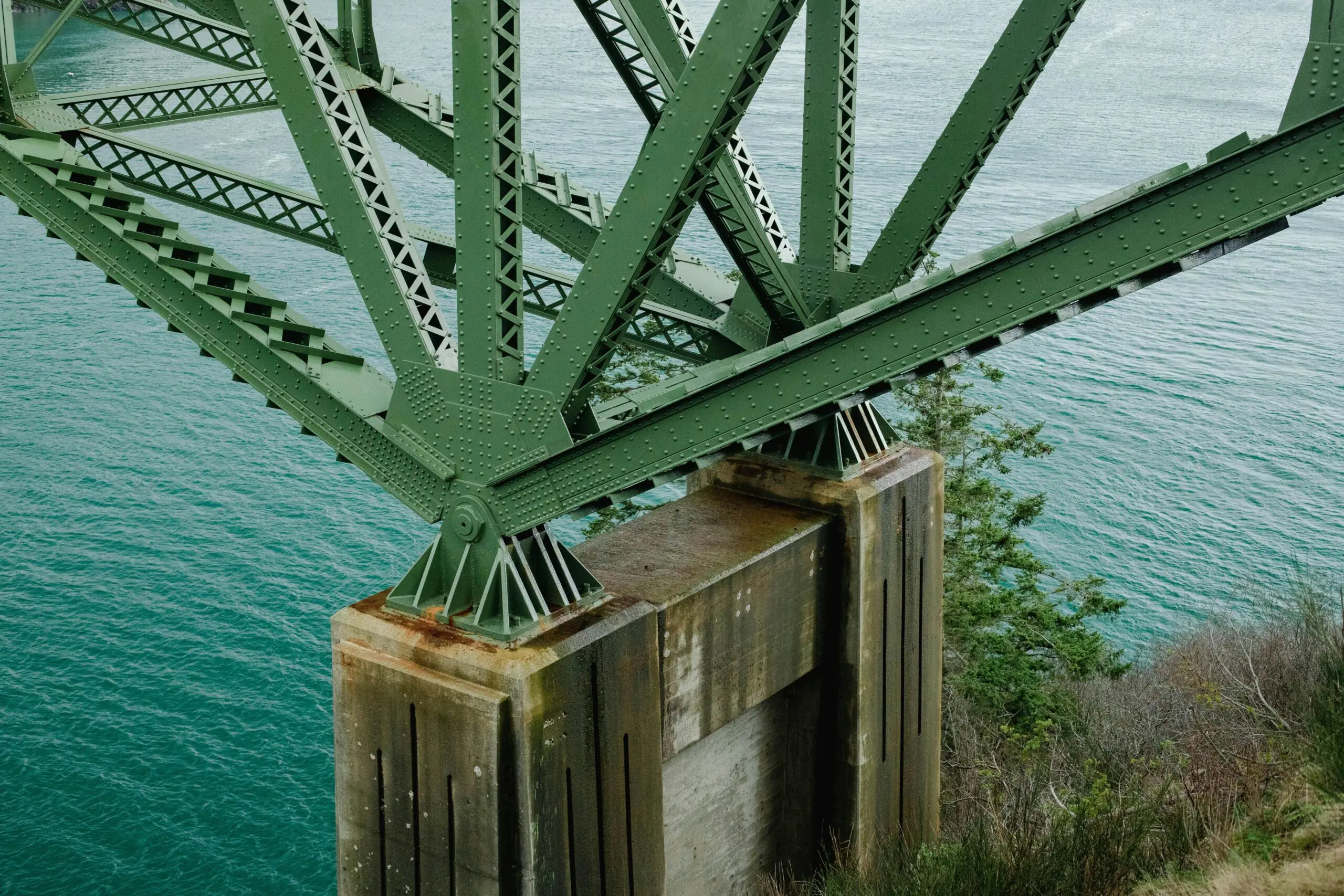The underside of a bridge showing green arches supporting the bridge above water.