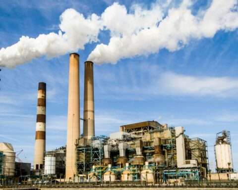 A power plant emitting carbon into the atmosphere before a blue sky.