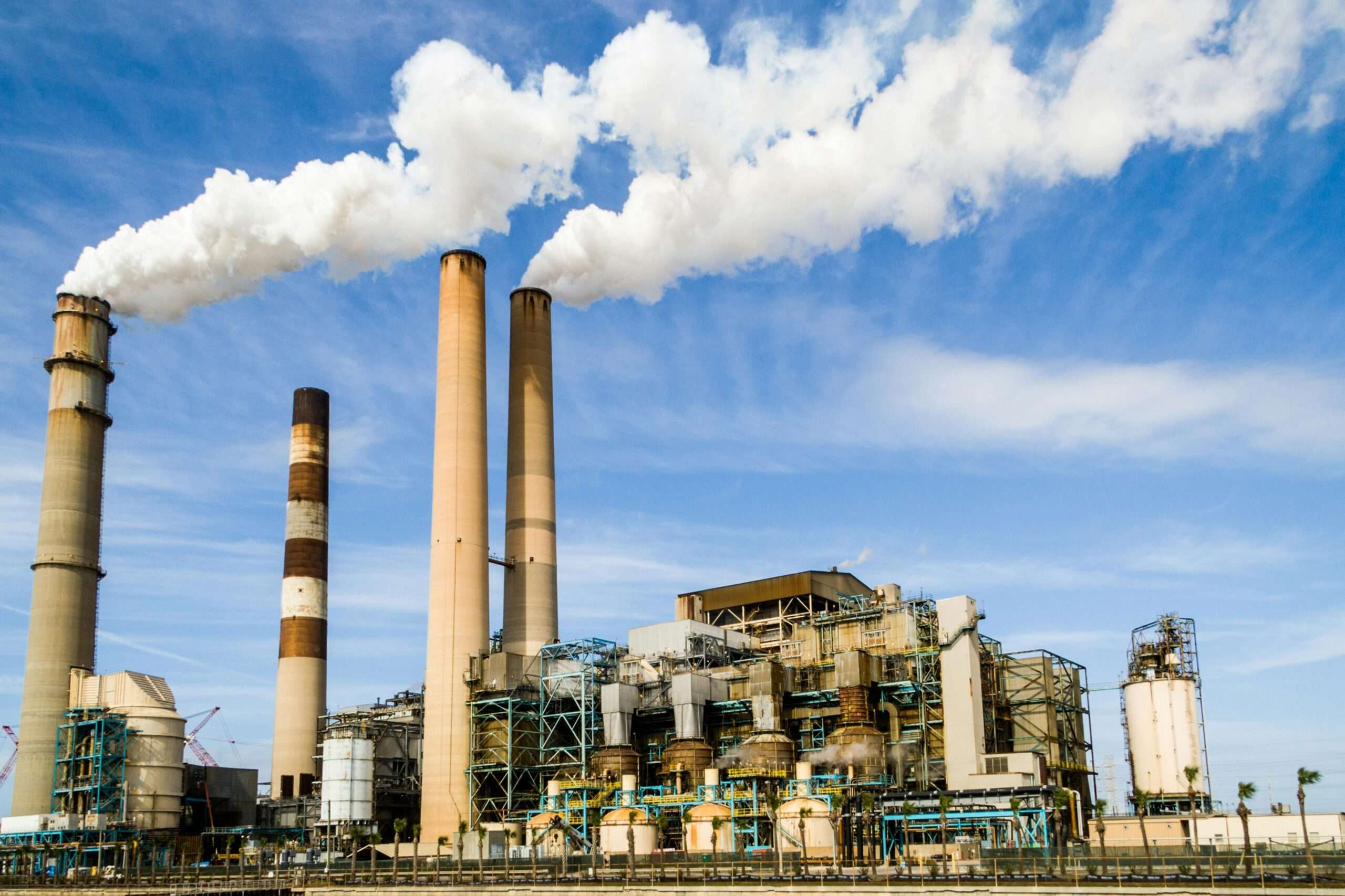 A power plant emitting carbon into the atmosphere before a blue sky.