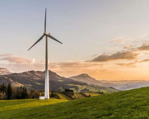 A wind turbine in an open field nearby rolling hills, distant water and a cloudy sky.