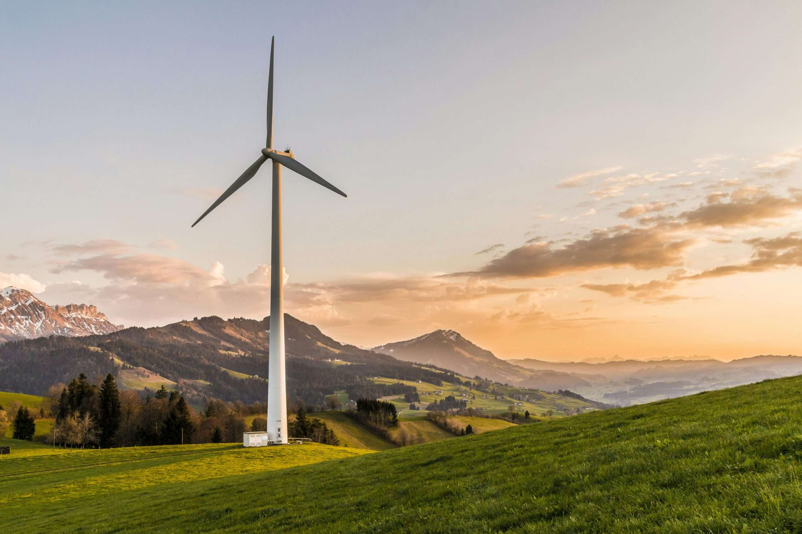 A wind turbine in an open field nearby rolling hills, distant water and a cloudy sky.