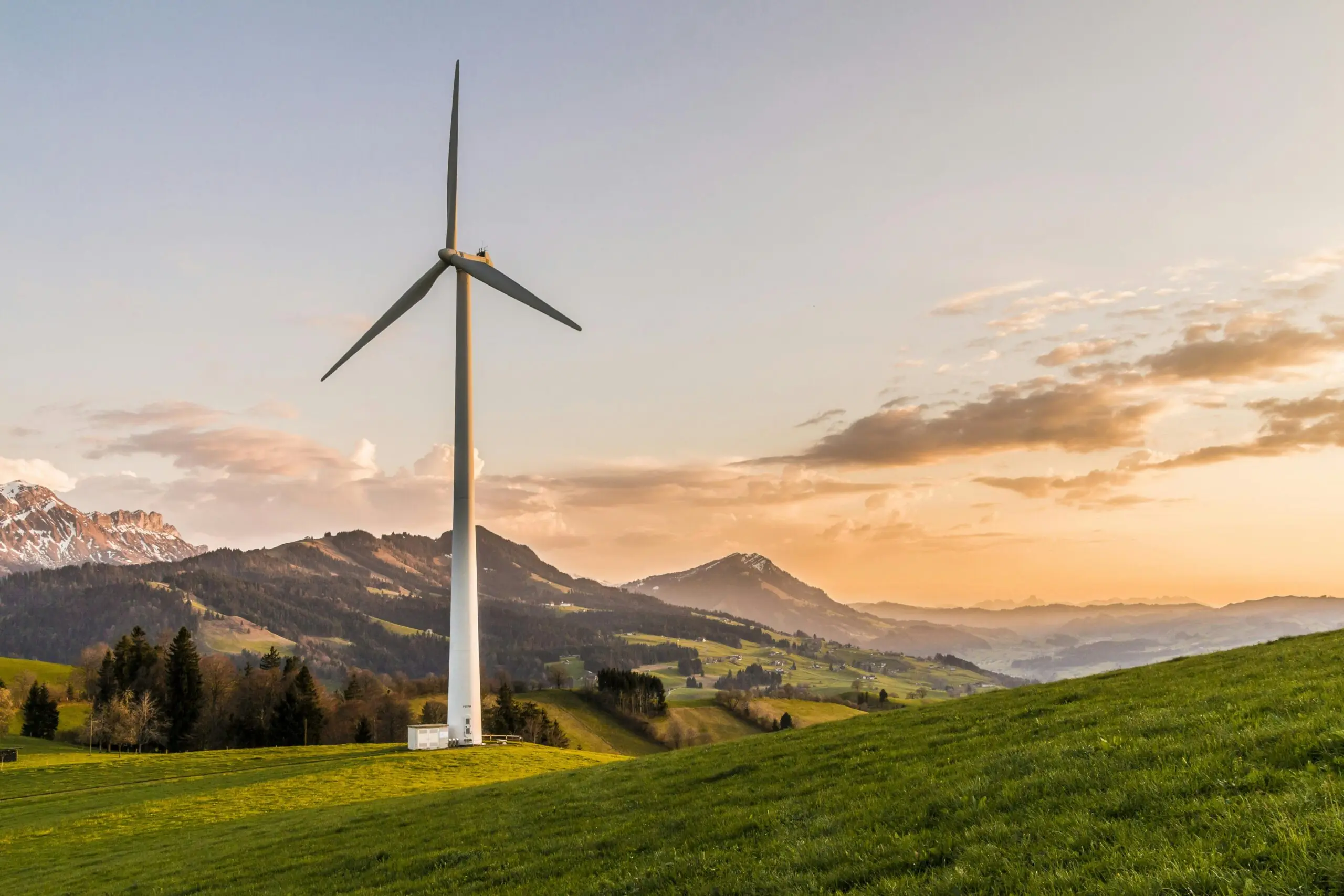 A wind turbine in an open field nearby rolling hills, distant water and a cloudy sky.