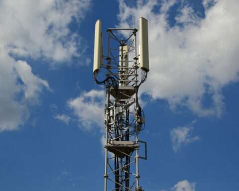 A tower connecting homes and businesses to internet before a cloudy blue sky.