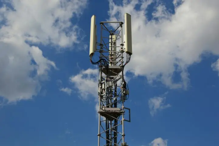 A tower connecting homes and businesses to internet before a cloudy blue sky.