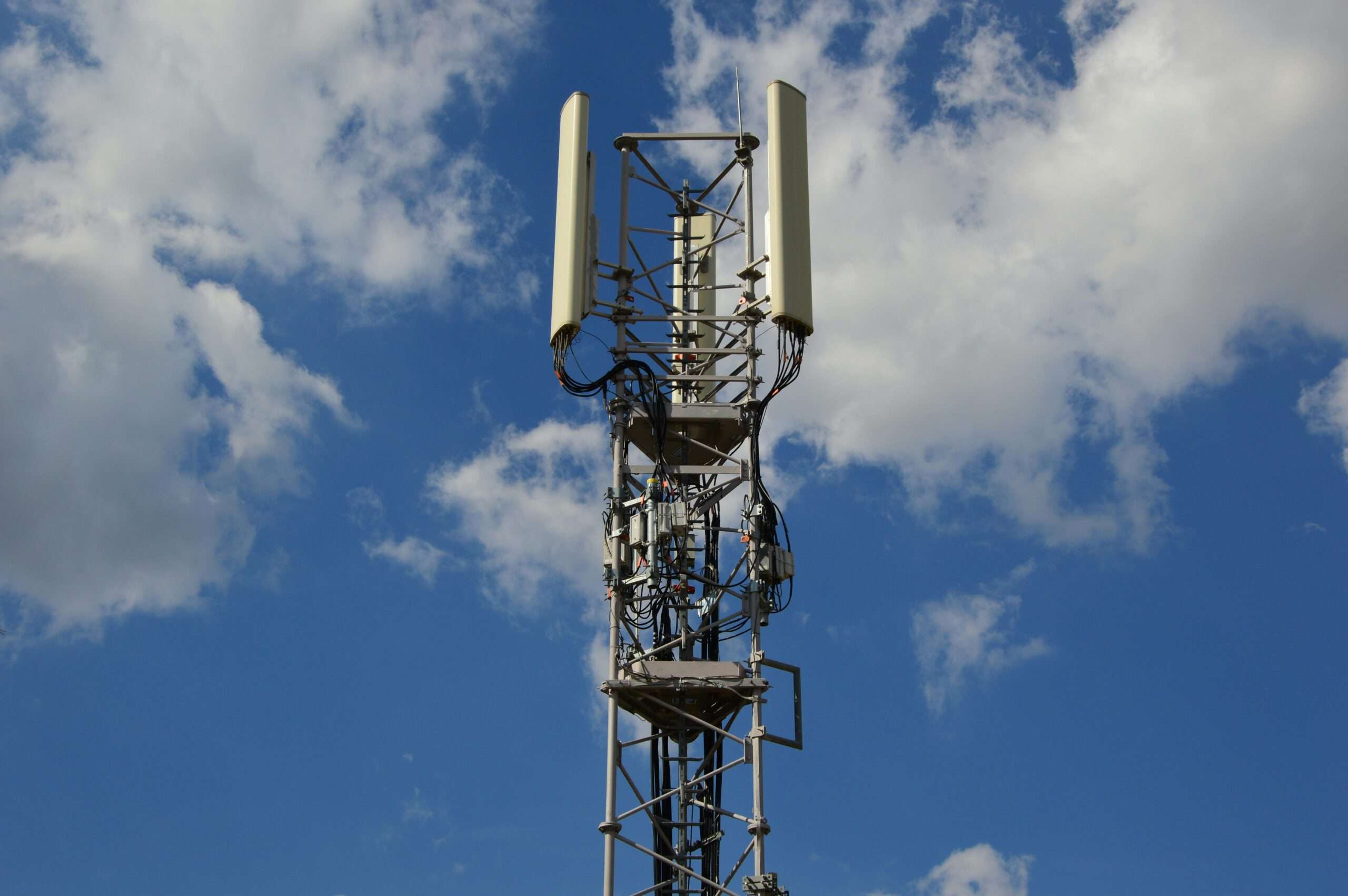 A tower connecting homes and businesses to internet before a cloudy blue sky.