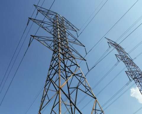 Electric transmission towers before a cloudy blue sky from teh ground.
