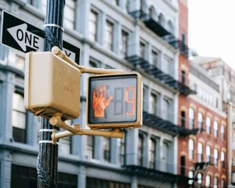 Digital signs on a traffic light along an intersection with residential housing building in the background.