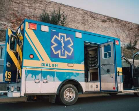 A blue ambulance with doors open alongside a street.