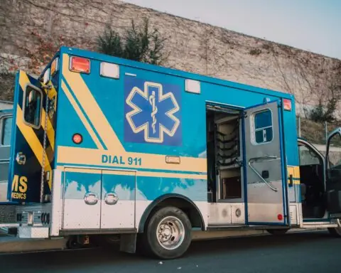 A blue ambulance with doors open alongside a street.