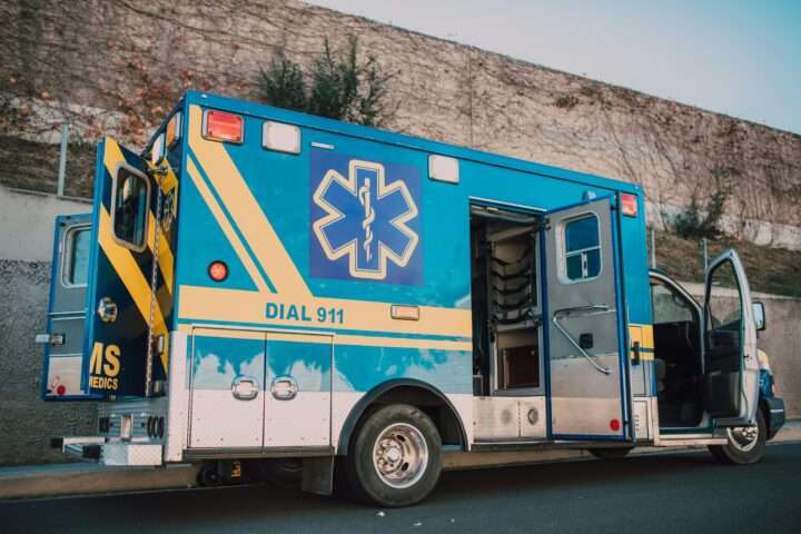 A blue ambulance with doors open alongside a street.