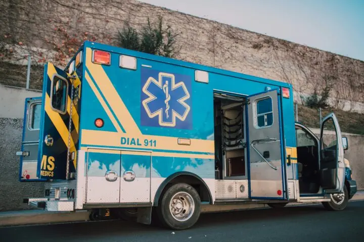 A blue ambulance with doors open alongside a street.