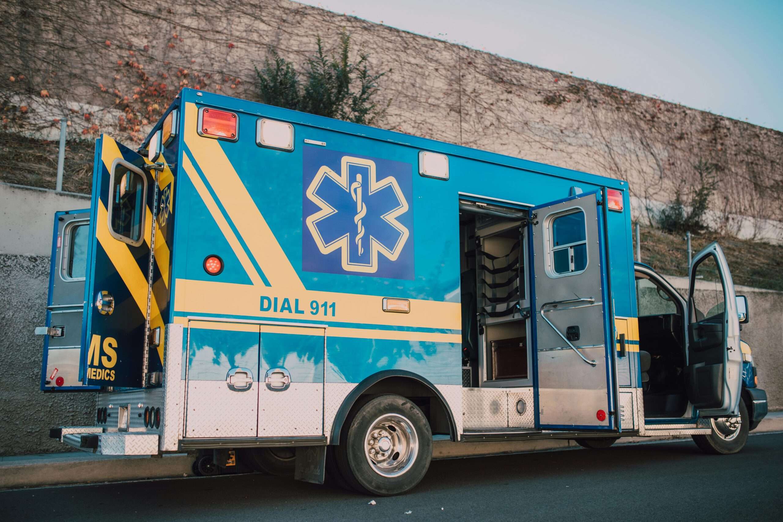 A blue ambulance with doors open alongside a street.