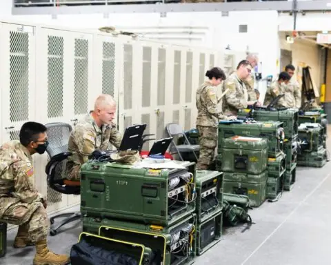 Air Force airmen and airwomen work on computers in front of lockers.
