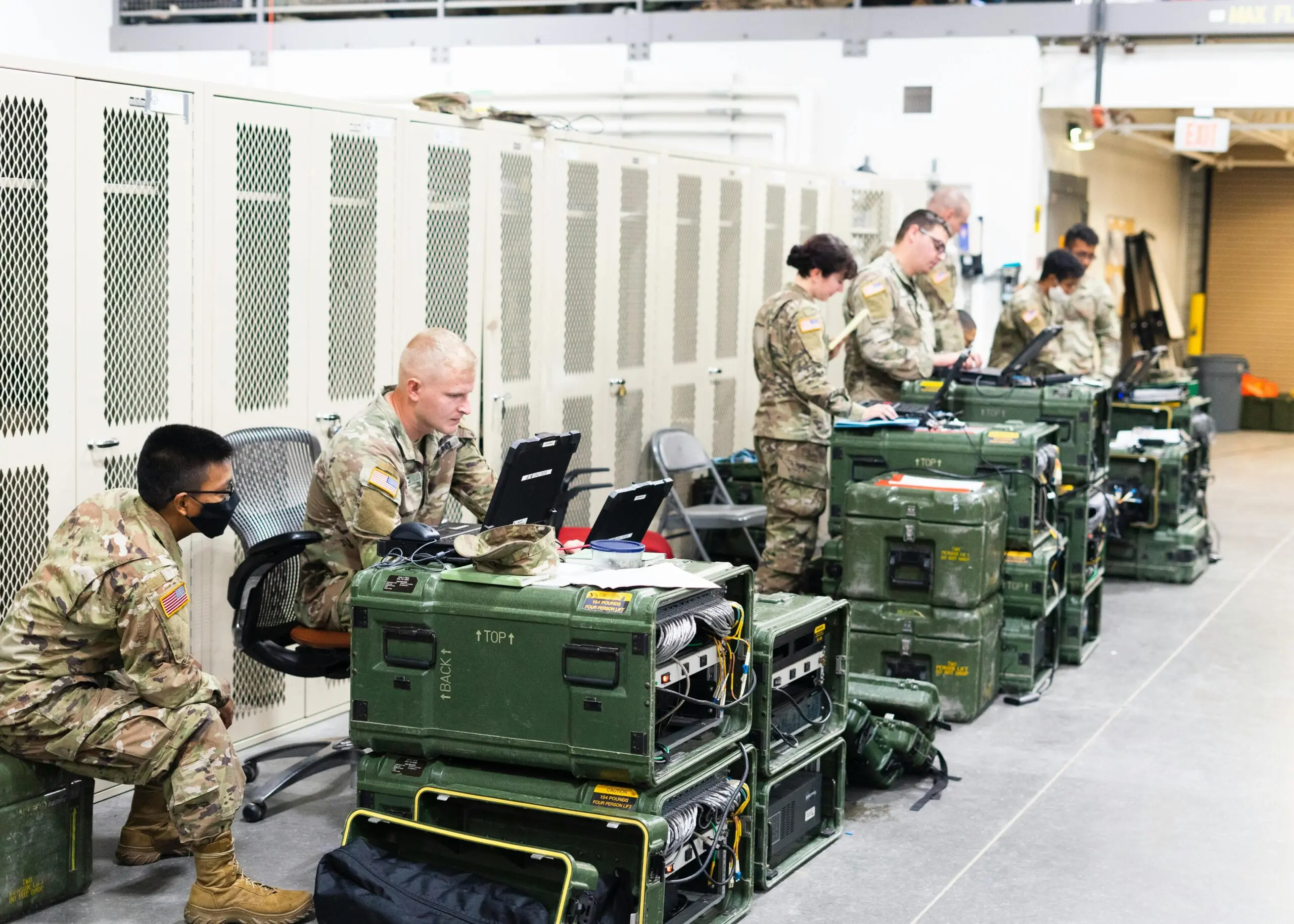 Air Force airmen and airwomen work on computers in front of lockers.