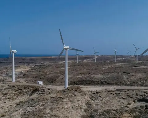 Several wind turbines generating clean energy before a blue sky and brown grass.