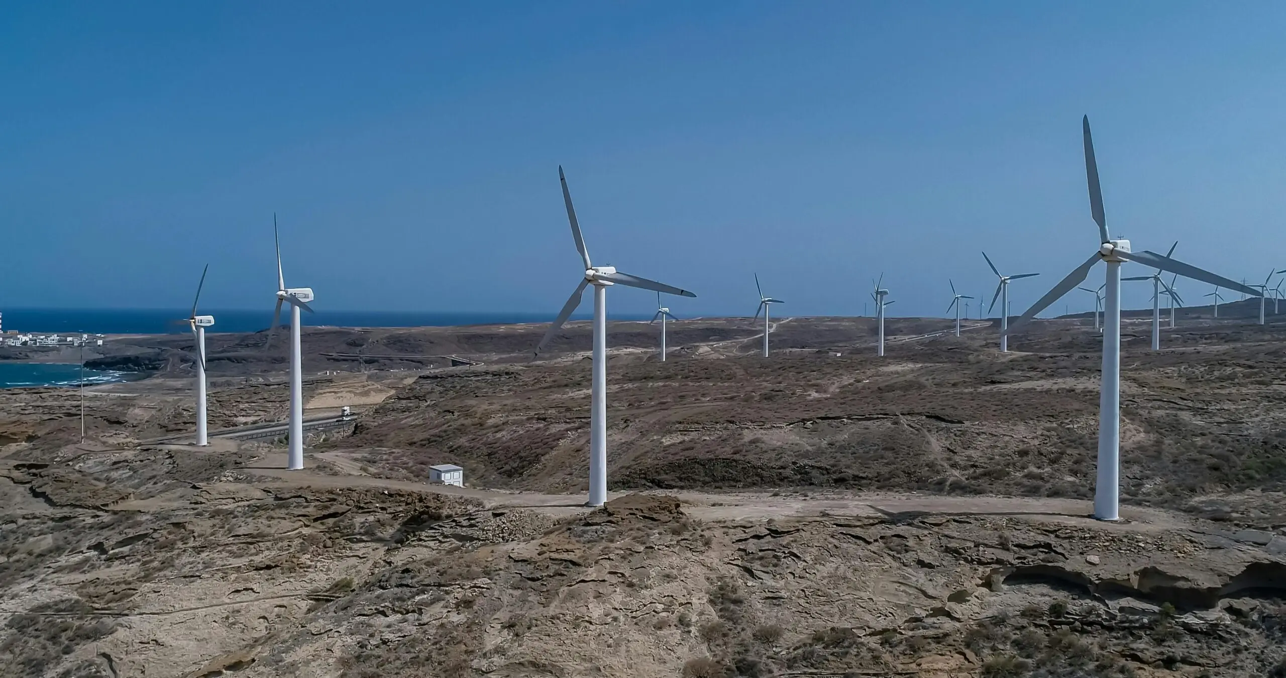 Several wind turbines generating clean energy before a blue sky and brown grass.