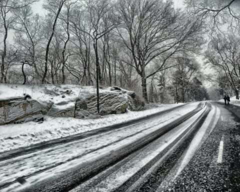A snowy road with people walking alongside during the day.