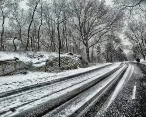 A snowy road with people walking alongside during the day.