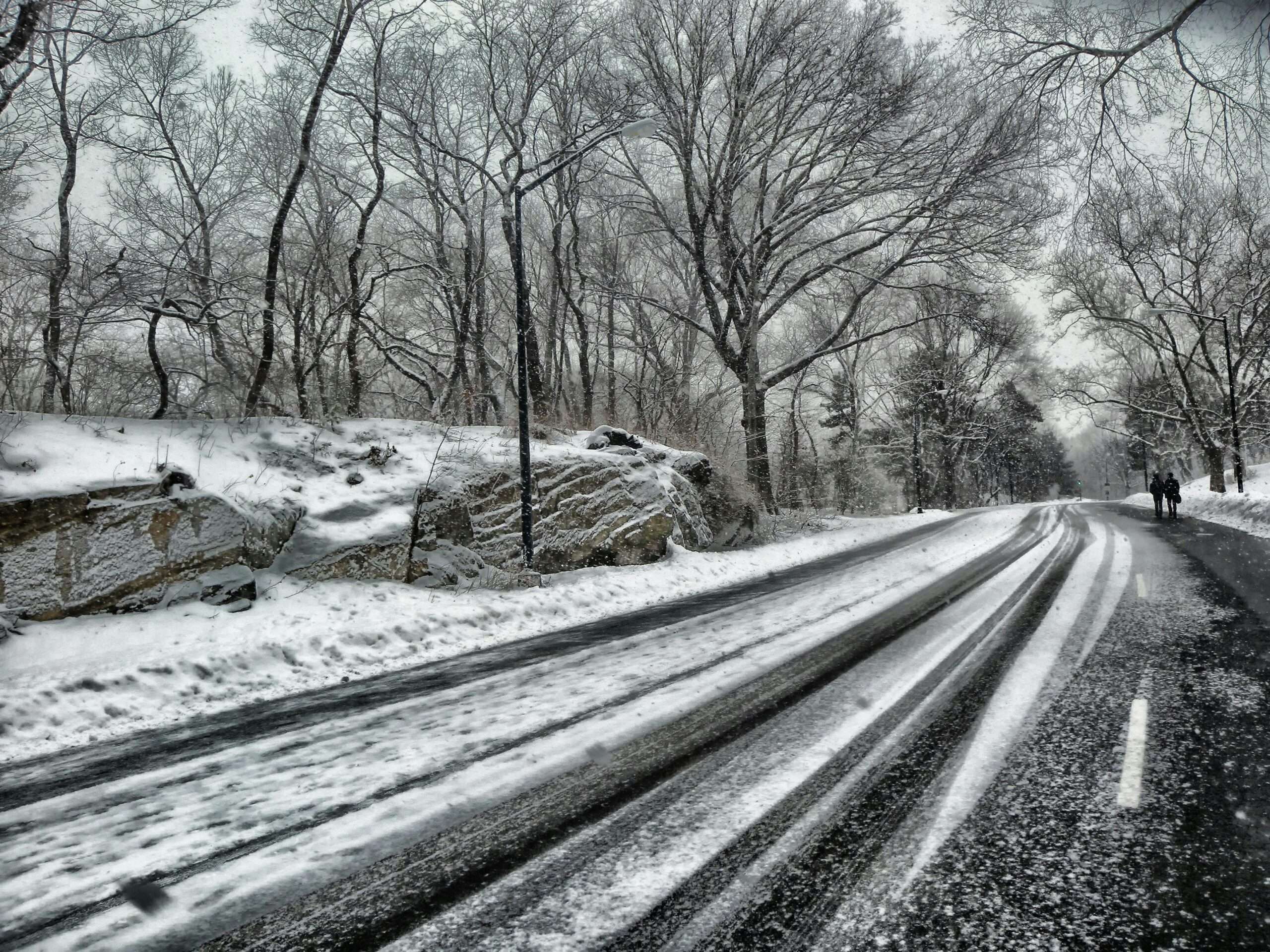 A snowy road with people walking alongside during the day.