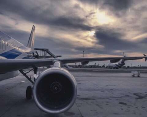 The wing of an airplane before a cloudy sky and tarmac.