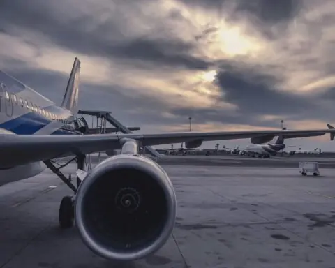 The wing of an airplane before a cloudy sky and tarmac.