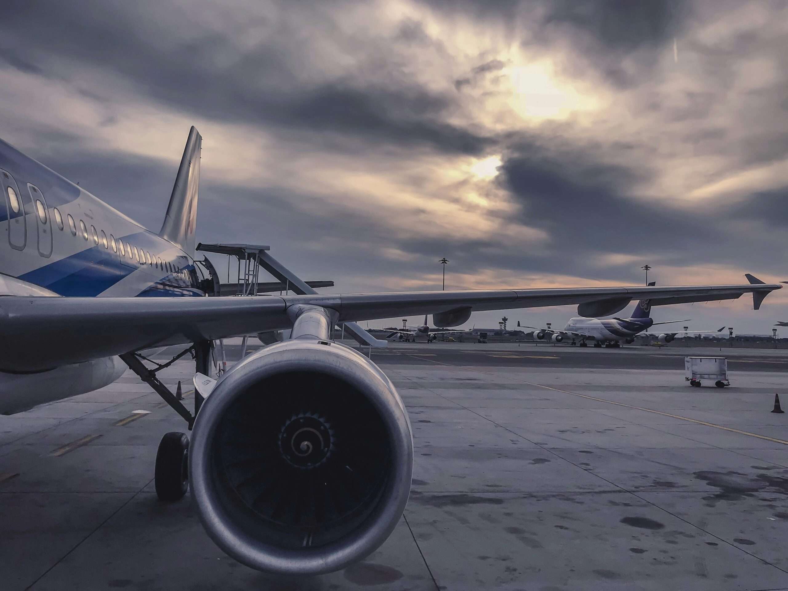 The wing of an airplane before a cloudy sky and tarmac.