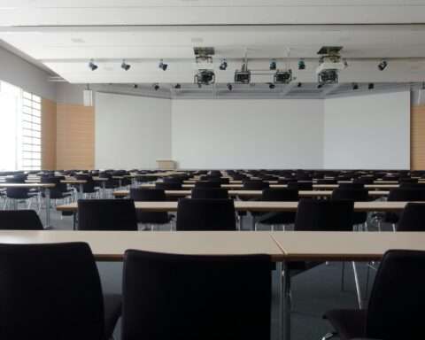 An empty classroom with projectors hanging from the ceiling and a large whiteboard at the front of the room.