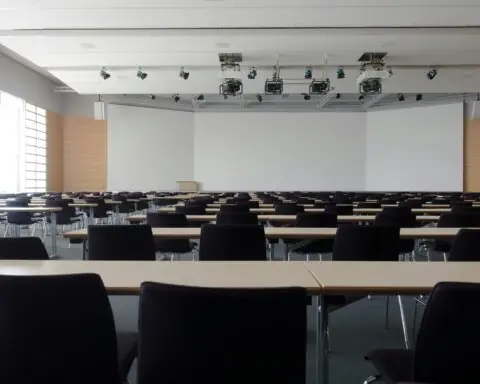 An empty classroom with projectors hanging from the ceiling and a large whiteboard at the front of the room.
