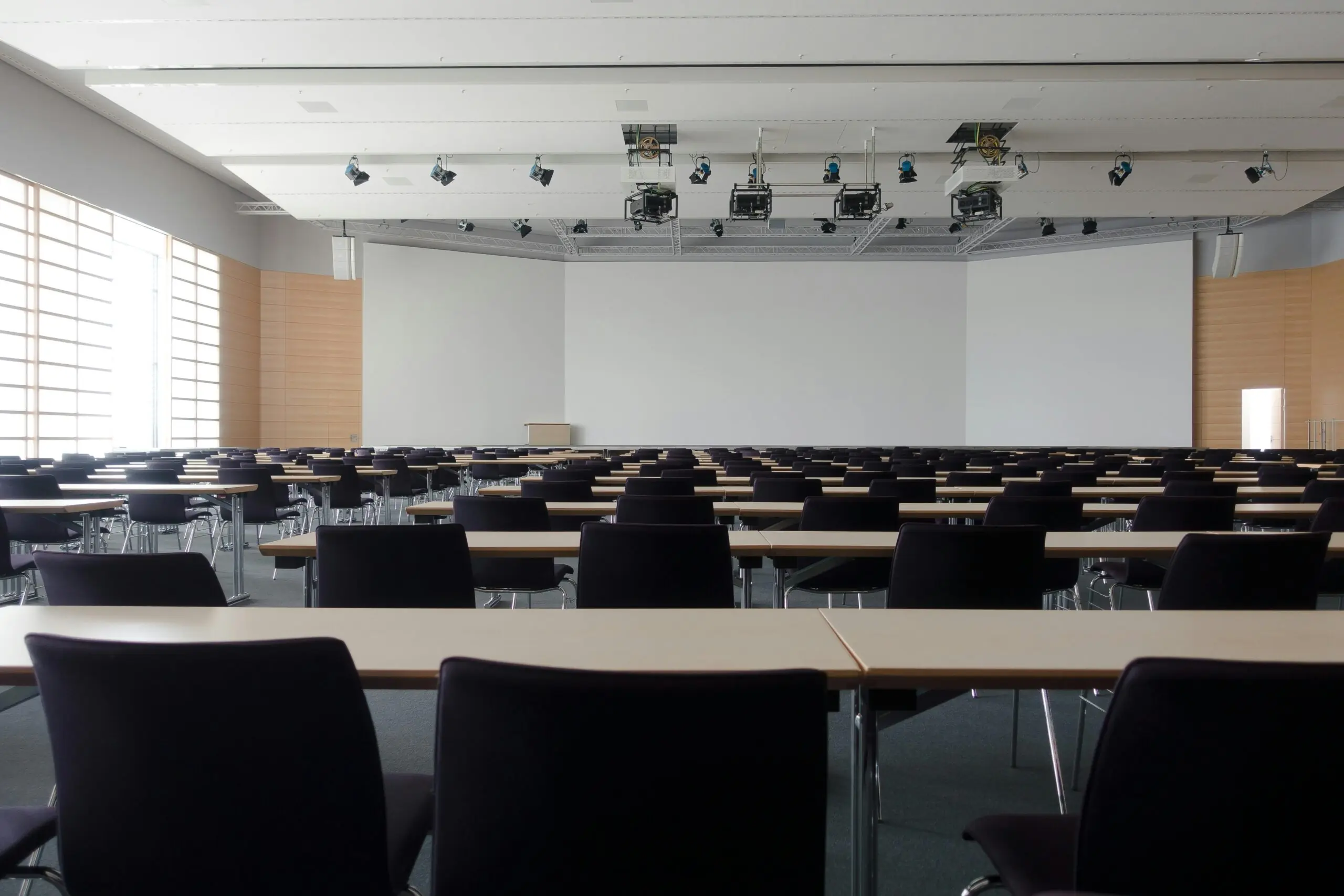 An empty classroom with projectors hanging from the ceiling and a large whiteboard at the front of the room.